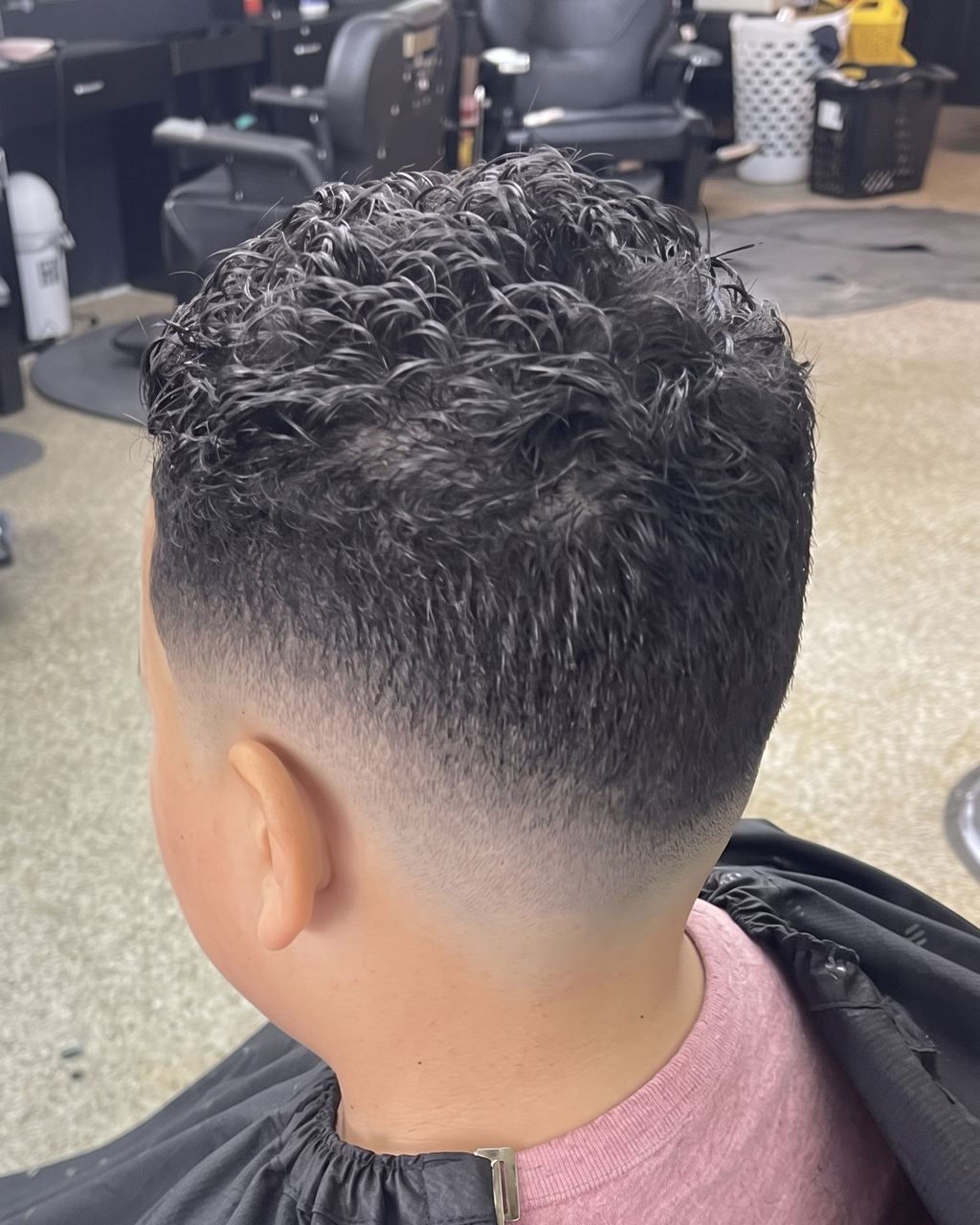 A textured curly top over a high skin fade, cut by Gio at Refined Barber Lounge, seen from behind in the chair.