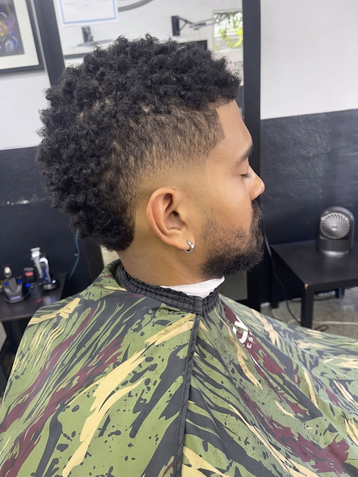 Side view of a high curly top over a skin fade, finished with a lined beard.