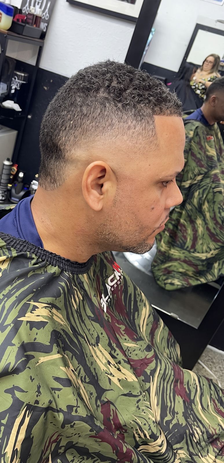 Side view of a salt-and-pepper curly top left long over a high taper fade.