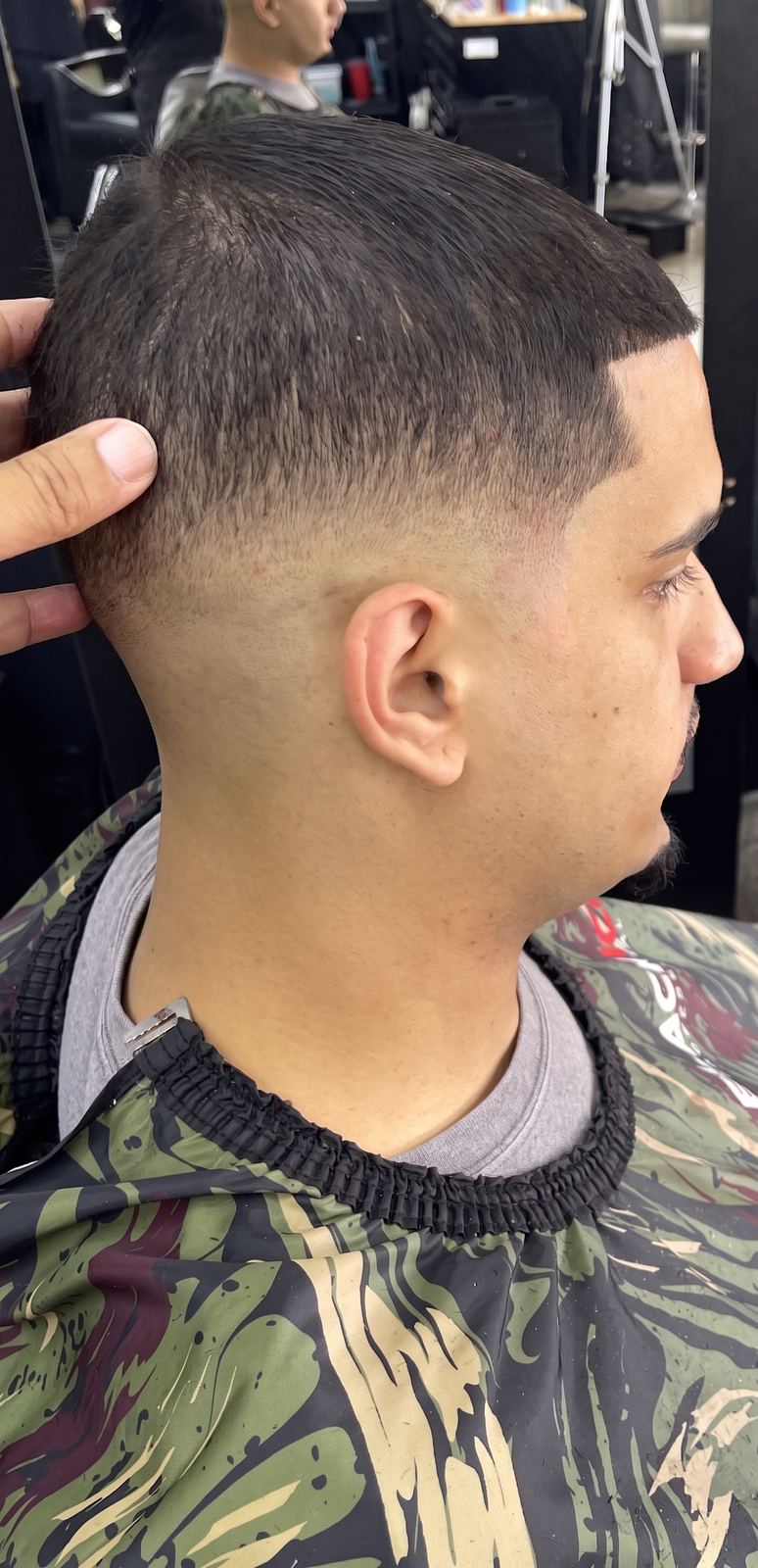 Rear three-quarter view of a taper fade at the nape, the barber’s hand steadying the head.